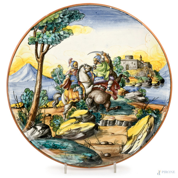Piatto in ceramica dipinta con lotta tra guerrieri, XX secolo, diametro cm 37, "G.B.T Made in Italy" (segni di usura, piccole cadute di smalto, difetti di cottura)
