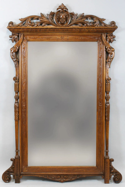 Specchiera in noce intagliata a motivi di foglie d&#39;acanto e grifoni, cimasa con volto di putto a rilievo, altezza 170x102 cm, XIX secolo.
