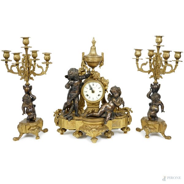 Trittico composto da orologio e due candelabri in bronzo dorato e brunito, Imperial, prima metà del XX secolo, decorati con putti, misure orologio cm h 46x40x16,5, (difetti, da revisionare)