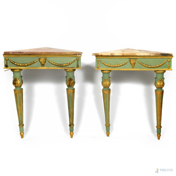 Coppia di consoline ad angolo in legno dipinto e dorato con piano in marmo giallo. Fronte arricchito da festoni e bucrani, XIX-XX secolo, cm 87,5x72x36 (difetti, rotture al piano, restauri, fori di tarlo, mancanze scalfiture)