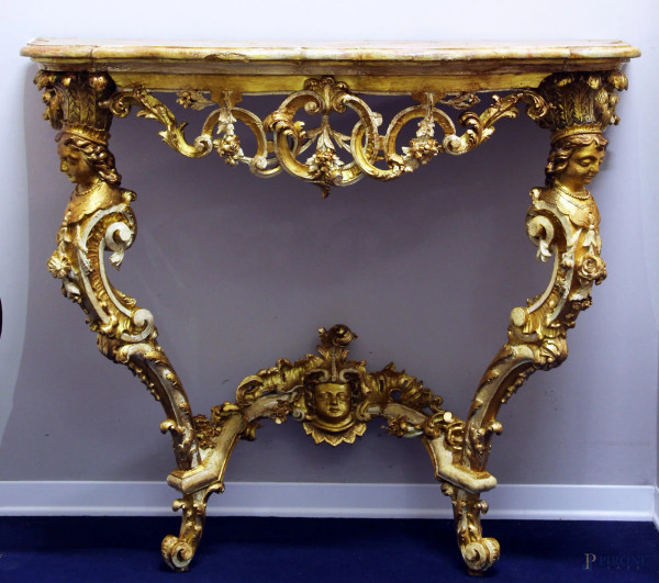 Consolina in legno intagliato e dorato di fine linea Luigi XV, piano di linea centinata in legno a finto marmo, poggiante su due gambe mosse con fiori e figure a rilievo, cm 100 x 105 x 51.