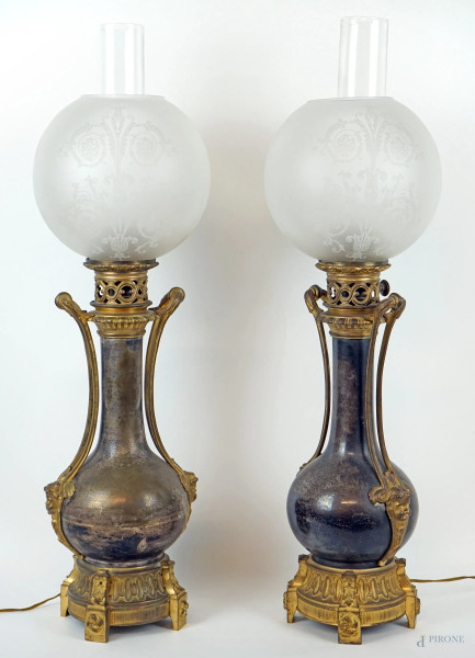 Coppia di lampade a petrolio in bronzo, prese con decoro a foggia di teste di cherubini e dettagli traforati, globi in vetro, XIX secolo,  cm h 65, (segni del tempo).