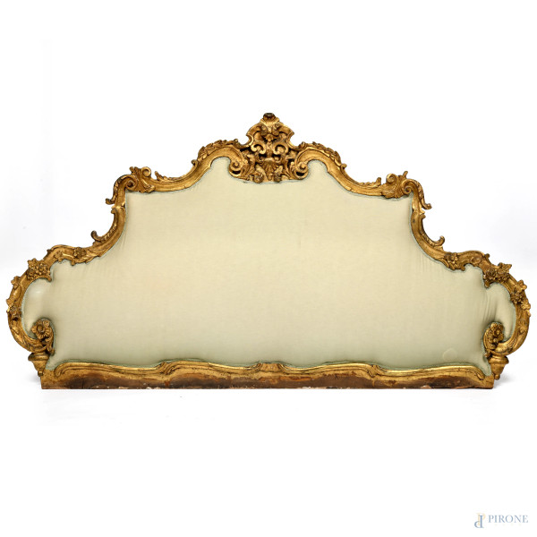 Testiera da letto con cornice in legno intagliato e dorato con imbottitura e rivestimento in tessuto nei toni del panna, XIX-XX secolo, cm 110x507, (segni di usura, scalfiture, restauri)