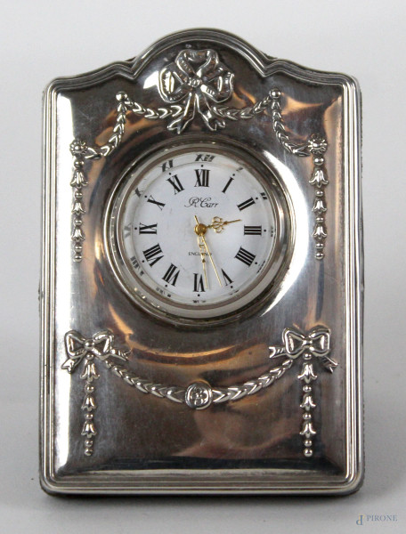Orologio da tavolo con cornice in argento di linea sagomata, decori raffiguranti fiocchi e festoni, cm h9,5x6,5x1