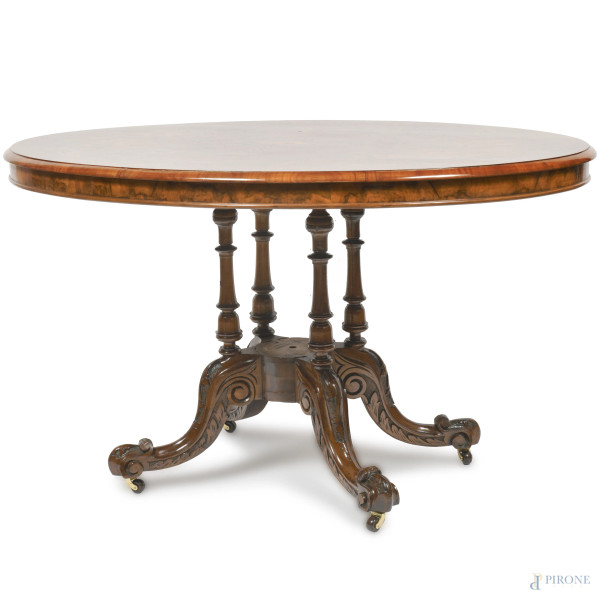 Tavolo a vela in noce con piano ovale intarsiato a motivi fitomorfi poggiante su fusto con quattro colonnine tornite raccordate da elemento circolare con quattro gambe mosse intagliate terminanti a ricciolo con rotelle, XX secolo, cm 84x134x104, (difetti)