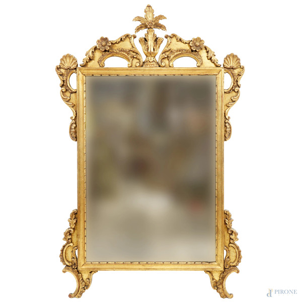 Specchiera in legno intagliato e dorato, XX secolo, con cornice scolpita a motivi rocailles, cm 131x84.