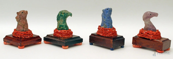 Lotto composto da quattro teste di animali diversi in pietre dure, contornate da coralli,poggianti su base in legno, H 7 cm.