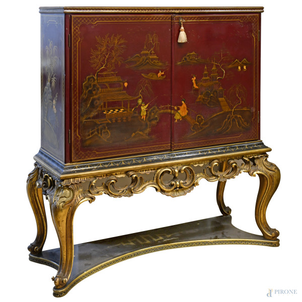 Mobile bar stile cinese a due sportelli in legno laccato rosso decoirato con personaggi in paesggio lacustre, su fregio in legno dorato e scolpito a volute e quattro gambe arcuate raccordate da pedana laccata nero e oro, XX secolo, cm 140x119,5x39,5, (difetti)