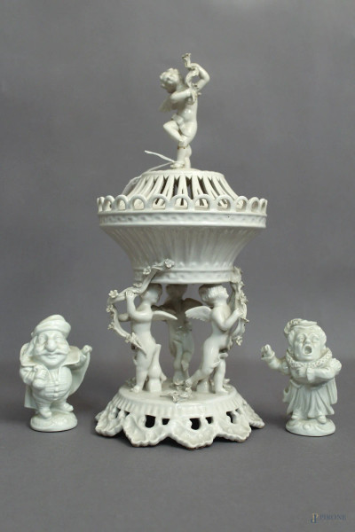 Lotto composto da un centrotavola in maiolica bianca sorretta da putti, H 35 cm, e da due sculture a soggetto di personaggi in porcellana Capodimonte, H 10 cm.