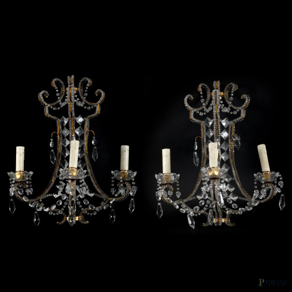 Elegante coppia di appliques a tre luci da parete in metallo dorato finemente lavorato e arricchite da molteplici elementi in cristallo. XX secolo, cm 46x34, difetti