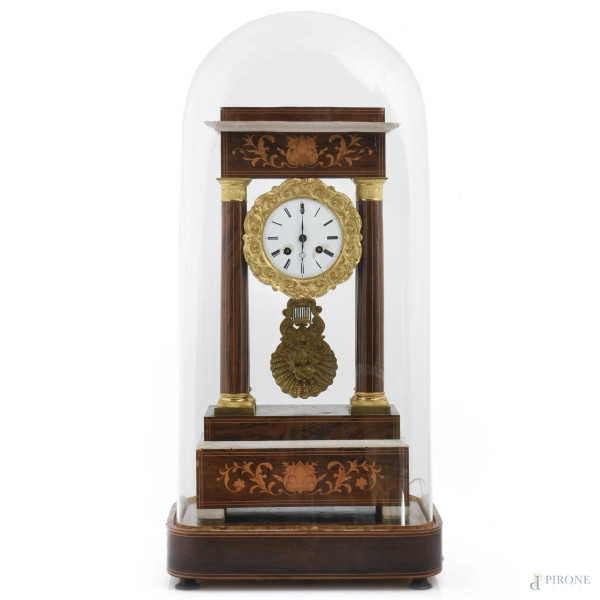 Orologio in stile Carlo X in legno impiallacciato e intarsiato con quadrante in bronzo dorato e smalto a numeri romani tra quattro colonne a fusto liscio, entro campana in vetro, XX secolo, misure complessive 65x31x20, (segni di usura, scalfiture, rotture, difetti, da revisionare)