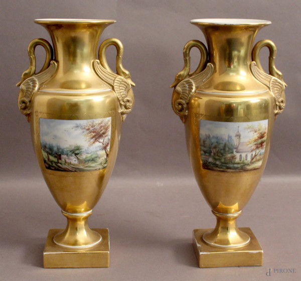 Coppia di vasi in porcellana dorata con anse a cigni e riserve dipinte a soggetti di paesaggi, Impero, H 34 cm.
