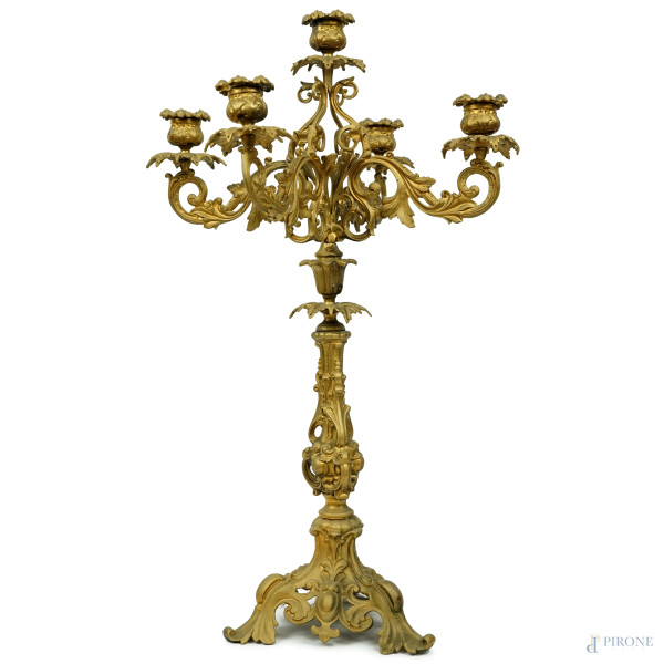 Candelabro in metallo dorato a cinque fiamme, XX secolo, cinque bracci a volute e bobeches fogliacee, fusto poggiante su base triangolare, cm h 54,(segni del tempo)