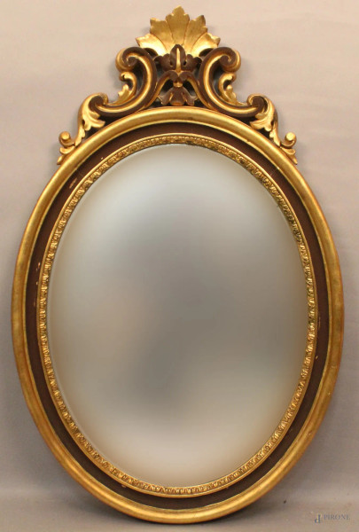 Specchiera di linea ovale in legno dorato, cimasa intagliata, H 105 cm.