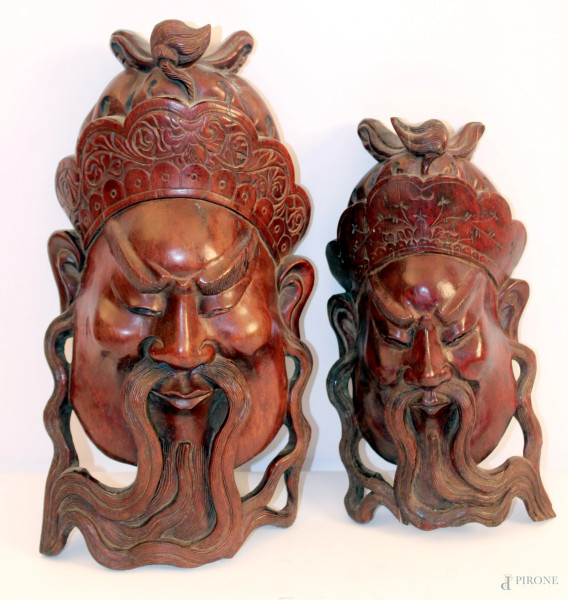 Lotto di due maschere in legno di teak intagliato raffiguranti volti orientali, Cina inizi XX sec, h.40 cm