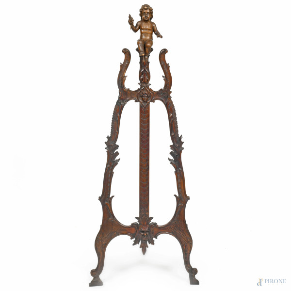Cavalletto in legno intagliato con scultura apicale di putto, XX secolo, altezza cm 147, (segni di usura, difetti, restauri, rotture, mancanze)