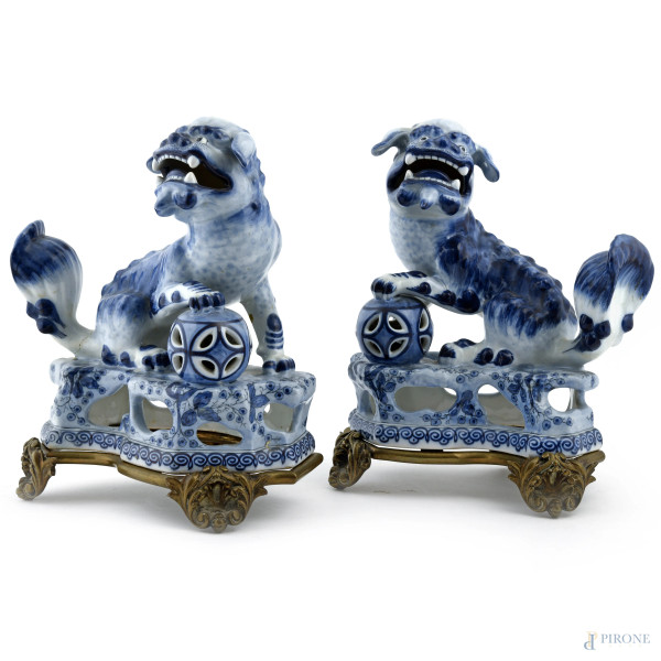 Coppia di cani di Pho in porcellana dipinta nei toni del blu con base in metallo dorato, XX secolo, misure massime cm 25x21x14, (segni di usura)