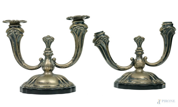 Coppia di candelabri a due luci in argento, XX secolo, decori sbalzati, basi in finto legno ebanizzato, cm h 18, (difetti, un braccio da saldare e mancanze)