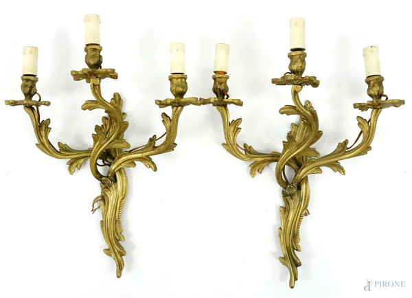 Coppia di appliques a tre luci in metallo dorato, bracci a volute, XX secolo, cm h 48x36, (lievi difetti).