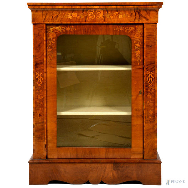Credenzina in radica di noce intagliata in varie essenze a motivi floreali. Singolo sportello a vetrina con triplice ripiano rivestito in tessuto. XX secolo, cm 106x75,5x31,5, (difetti)