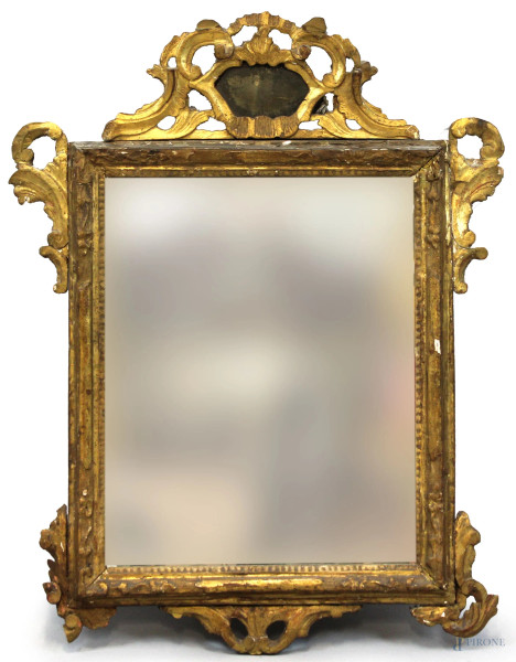 Specchiera in legno intagliato e dorato, XVIII secolo, cornice scolpita a racemi e volute vegetali, cimasa centrata da piccolo specchio a cartiglio, cm 88x68, (difetti)
