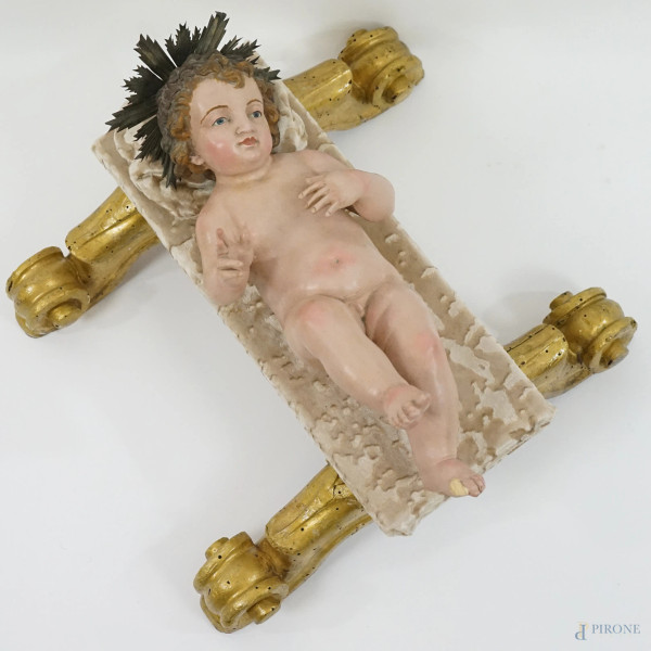 Gesù Bambino, scultura da presepe in legno policromo con occhi in vetro ed aureola in lamina d'argento, cm h 13x37x16, Napoli, XIX secolo, base in legno dorato su quattro piedini a ricciolo, inserto e cuscinetto in velluto color tortora, ingombro della base cm 13x34x40, (difetti)