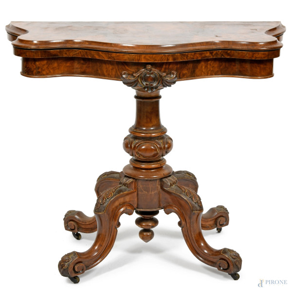 Tavolo da gioco impiallacciato in radica poggiante su fusto centrale tornito terminante in tre gambe mosse intagliate. Piano apribile celante area da gioco circolare in velluto verde. XX secolo, cm 73x90x44, piano aperto cm 90x90, (graffi, segni di usura)