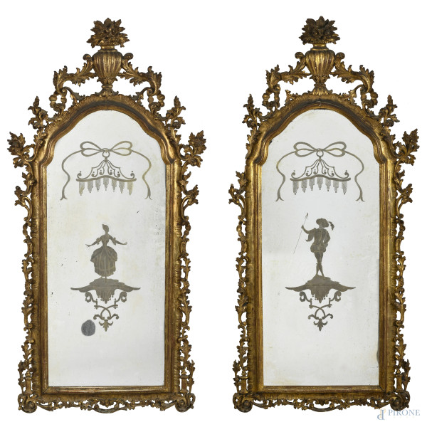 Coppia di specchiere in legno dorato e intagliato a volute vegetali. Specchio inciso con figure in costume. XX secolo, cm 115x55, (segni di usura, scalfiture, difetti)