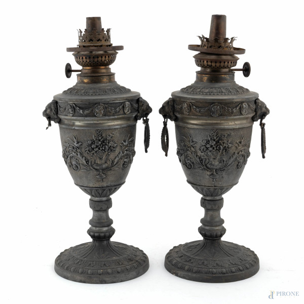 Coppia di lampade ad olio in antimonio a guisa di urna con rilievi di teste leonine e candelabre, XX secolo, altezza cm 34, (segni di usura, difetti, mancanze, da revisionare)