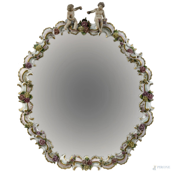 Specchiera con cornice in porcellana dipinta e smaltata a motivi floreali. Elementi apicali a guisa di putti, XX secolo, cm  76x60, (segni di usura, rotture, difetti)