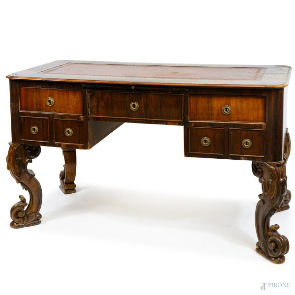 Tavolo scrittoio in legno impiallacciato, XIX secolo, piano con inserto in pelle rossa, fronte a sette cassetti con pianetto estraibile, quattro gambe riccamente scolpite, cm h 136x82.5x66, (difetti e restauri)