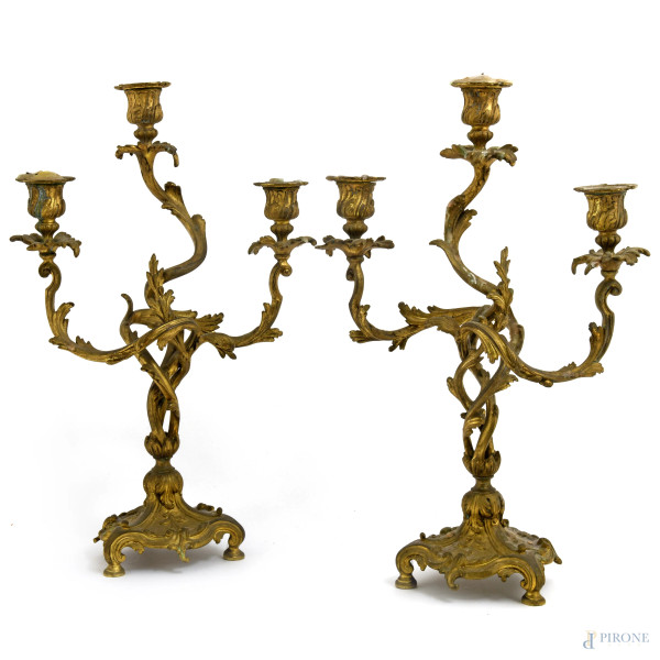 Coppia di candelieri a tre fiamme in bronzo dorato, riccamente decorati con volute vegetali, XX secolo, cm 42x27