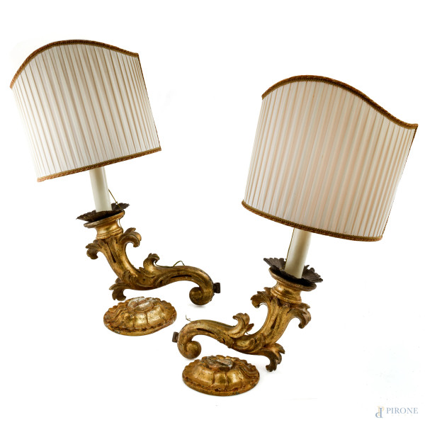 Coppia di appliques in legno intagliato e dorato a una luce con paralume in tessuto color avorio, XX secolo, misure comprensive di paralume cm 77x34 circa , (segni di usura, scalfiture, perdita di doratura, difetti)