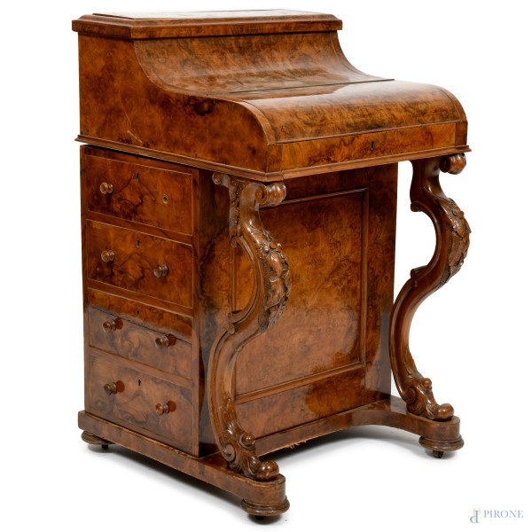 Davenport impiallacciato in radica, composto da corpo superiore con anta a ribalta celante vano scrittoio a scorrimento con piano in pelle verde, scomparti porta oggetti e coppia di cassettini. Base con quattro cassetti in colonna da ambo le parti del mobile. Supporti in legno riccamente intagliato a volute. XIX secolo, cm 89x56x56 (segni di usura, cassetti interni sostituiti)