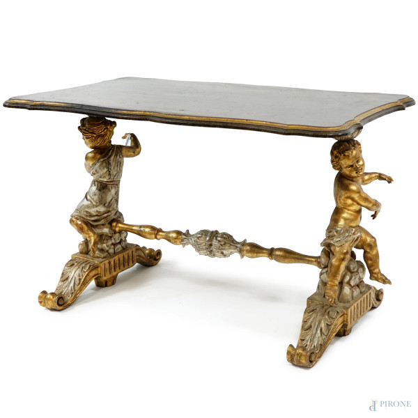 Tavolino basso in legno intagliato, dorato e argentato, piano mistilineo e montanti a foggia di putti, XX secolo, cm h 55x54x98 (difetti)