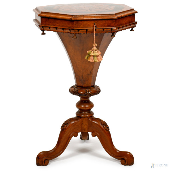 Tavolinetto da centro di forma ottagonale impreziosito da ricco intarsio centrale decorato con motivo floreale e volute stilizzate, apribile a ribalta e celante vano conico e scomparti con rivestimento in tessuto. Fusto centrale tornito che si innesta su tre gambe terminanti a volute, XIX-XX, cm 76x51, (difetti)
