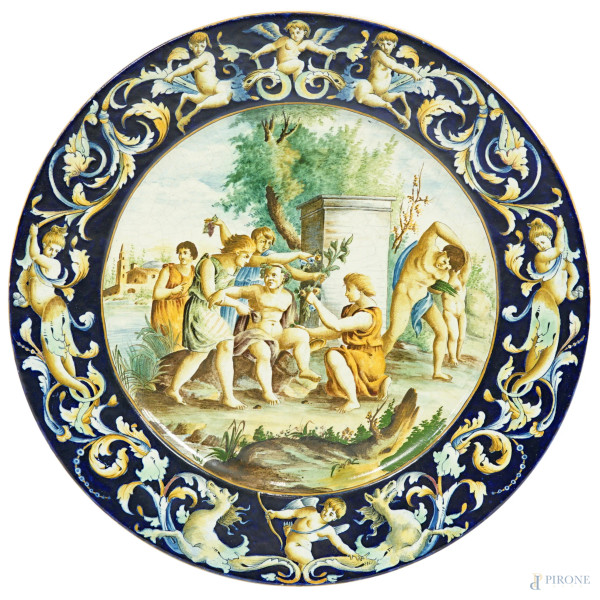 Grande piatto in maiolica policroma dipinta e smaltata, cavetto raffigurante una scena bacchica, tesa con decoro a grottesche su sfondo blu, fine XIX secolo, diam. cm 49 (difetti)