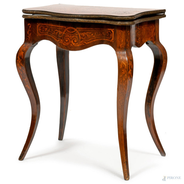 Tavolo da gioco in legno intagliato in varie essenze con profilo e gambe mosse. Piano apribile  e rotante con rivestimento interno in velluto verde. Vano interno diviso in scompartimenti, XIX-XX, cm 72x60x37. Piano aperto cm 79x60, (difetti)