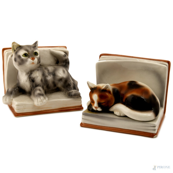 Coppia di fermalibri in porcellana policroma a foggia di gatti adagiati su libri, XX secolo, misure massime 16x18x14, (difetti)