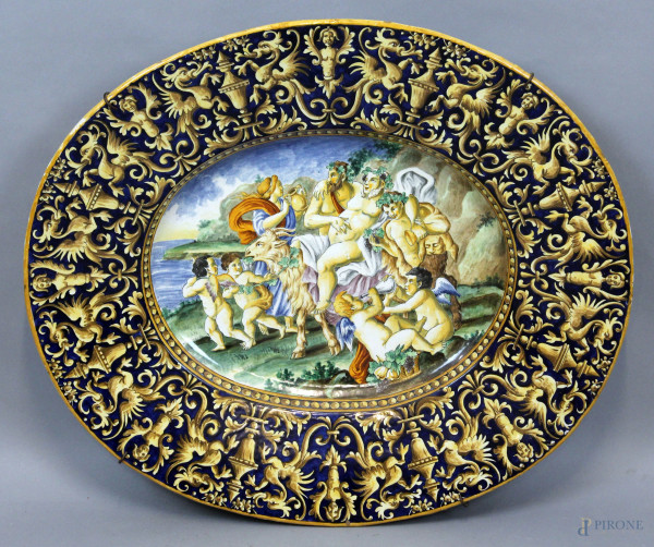 Grande piatto di linea ovale in ceramica policroma, con decoro raffigurante il Trionfo di Bacco, bordo a grottesche e motivi vegetali, cm 63x54, XIX secolo, (difetti)