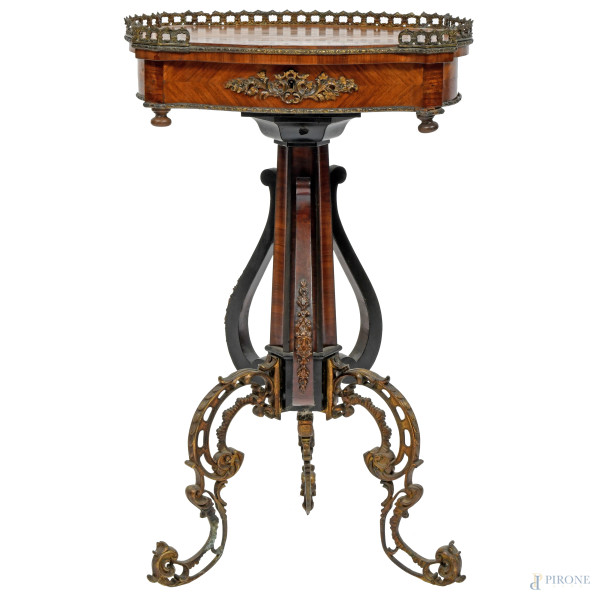 Tavolinetto tripode da toletta impiallacciato e intarsiato in varie essenze con inserti in bronzo dorato e gambe a ricciolo. Piano apribile celante specchio ovale e vano ripartito. Francia, XX secolo, cm 70x43x33, (segni di usura)