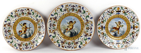 Tre piatti da parete in maiolica policroma, cavetti decorati con puttini, tesa a grottesche, diametro max cm. 30,5, XX secolo.