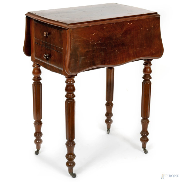 Tavolo a bandelle impiallacciato in mogano. Lati scanditi rispettivamente da due cassetti e uno sportello a ribalta. Gambe munite di rotelle. XX secolo, chiuso cm 71x37,5x52; aperto cm 71x72x52, (graffi al piano, sollevamento dell'impiallacciatura)