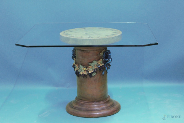 Tavolo con piano in cristallo, (difetti), poggiante su base in terracotta con festoni a rilievo, h. 72x118x118 cm.