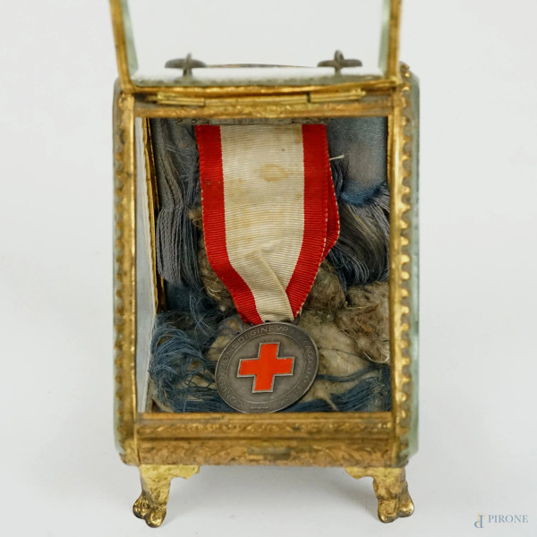 Medaglia Croce Rossa Italiana, in metallo argentato e smalto rosso, diam. cm 2,5, entro teca.