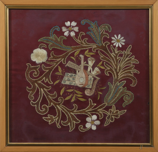 Composizione a ricamo con elementi floreali e strumenti musicali su tessuto, XX secolo, cm 41x43, entro cornice, (segni di usura)