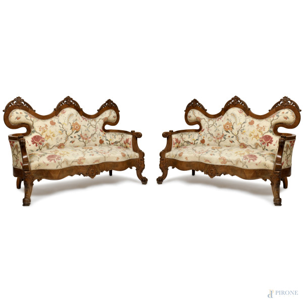 Coppia di divani tre posti in noce intagliato a volute vegetali, gambe anteriori mosse, piedi e braccioli a ricciolo, rivestimento in tessuto a motivi floreali, XIX secolo, 108x160x64, (usura del tempo)