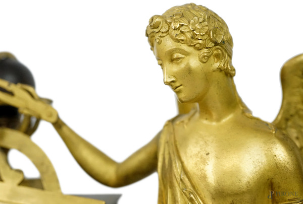 Pendola da tavolo in metallo brunito e dorato, XX secolo, quadrante affiancato da figura alata co...