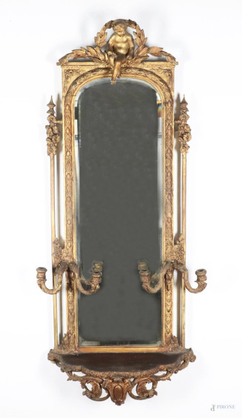 Specchiera con mensola in legno dorato e intagliato. Cimasa con scultura di putti e due portacandele a due luci ai lati, XIX secolo, cm 126x56x19, (segni di usura, scalfiture, graffi, cadute di doratura, rotture, restauri, specchio molato non pertinente)