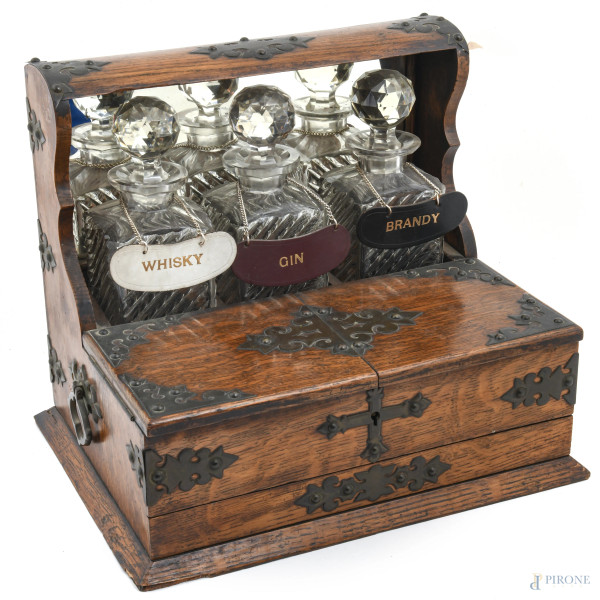 Servizio da liquore con struttura in rovere con inserti in metallo a doppia anta celante vano, un cassettino e fondo specchiato. Completo di tre bottiglie in cristallo, XX secolo, misure complessive della struttura cm 32x27x37, (segni di usura, difetti, s